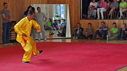 Maister Yu muossa ün exercizi cun üna spada. Corsin Biert (a schnestra), üna traductura e maister Liu observan al muong. Eir il public es fich interessà (fotografias: Selina Bisaz).