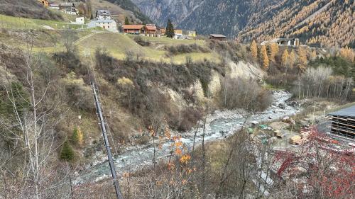 Auf dem Bild ist die Örtlichkeit zu sehen, wo der Mann gefunden werden konnte. Man sieht den Bach Brancla, Wiesland, Bäume, einige Häuser von Ramosch und die Bergwelt (Foto: Kantonspolizei Graubünden). 